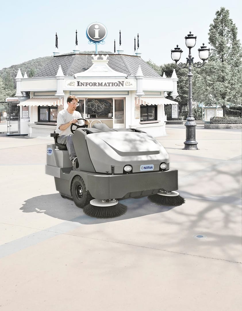 Ride-on industrial sweeper cleaning outdoor pathways at a theme park