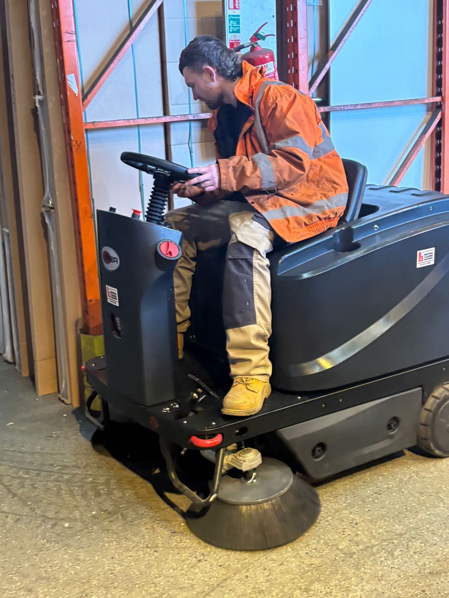 Ride-on industrial sweeper cleaning warehouse floor
