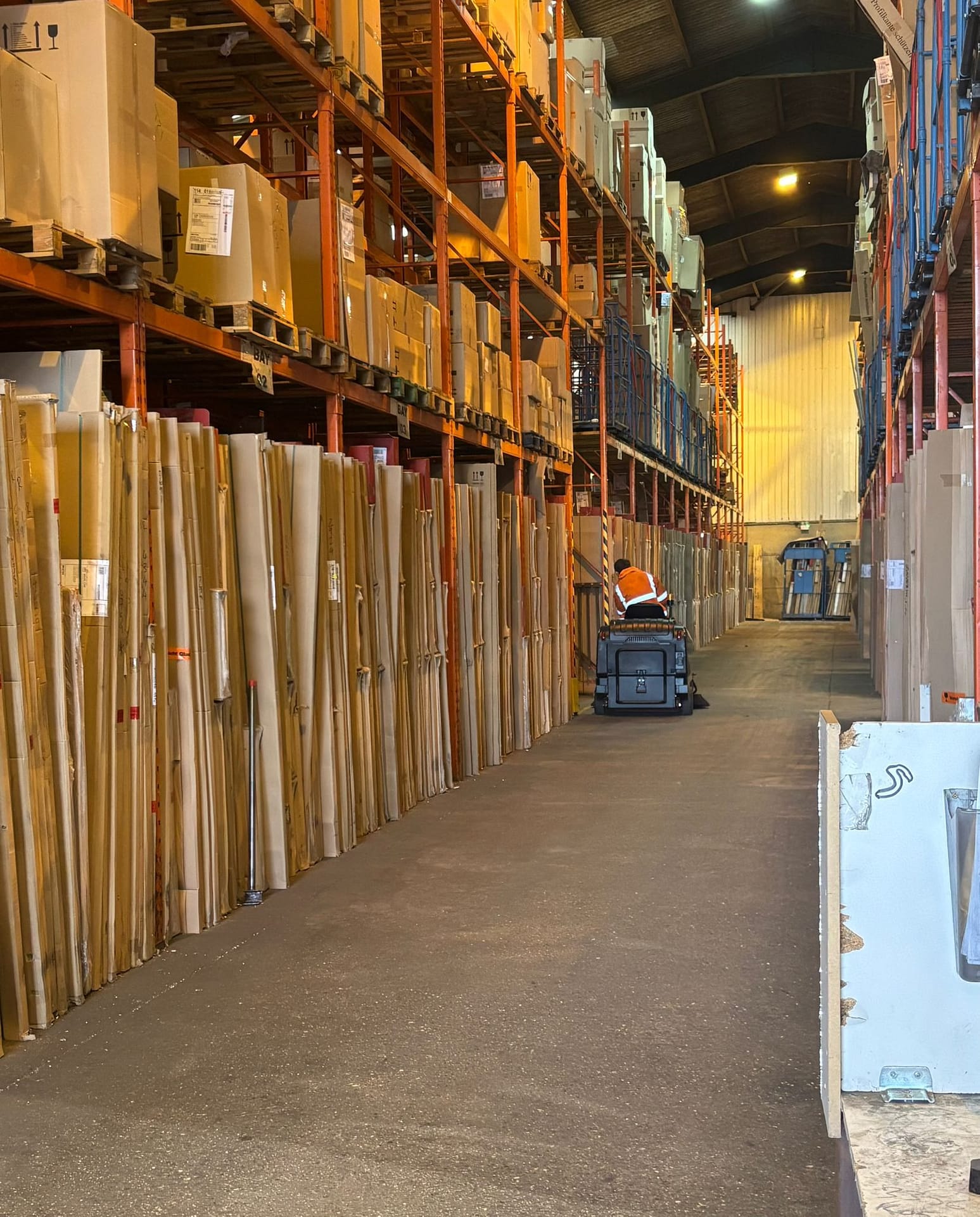 Ride-on industrial sweeper cleaning warehouse aisle