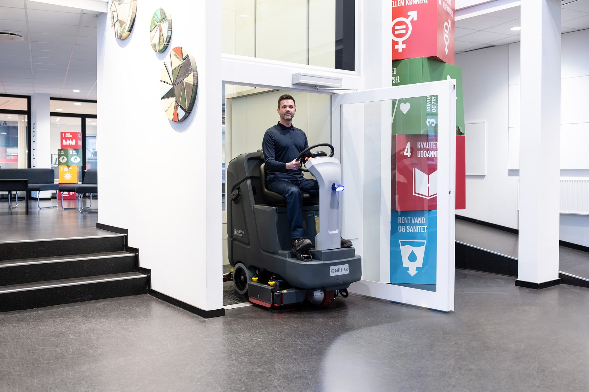Nilfisk SC4000 compact ride-on scrubber dryer near a lift